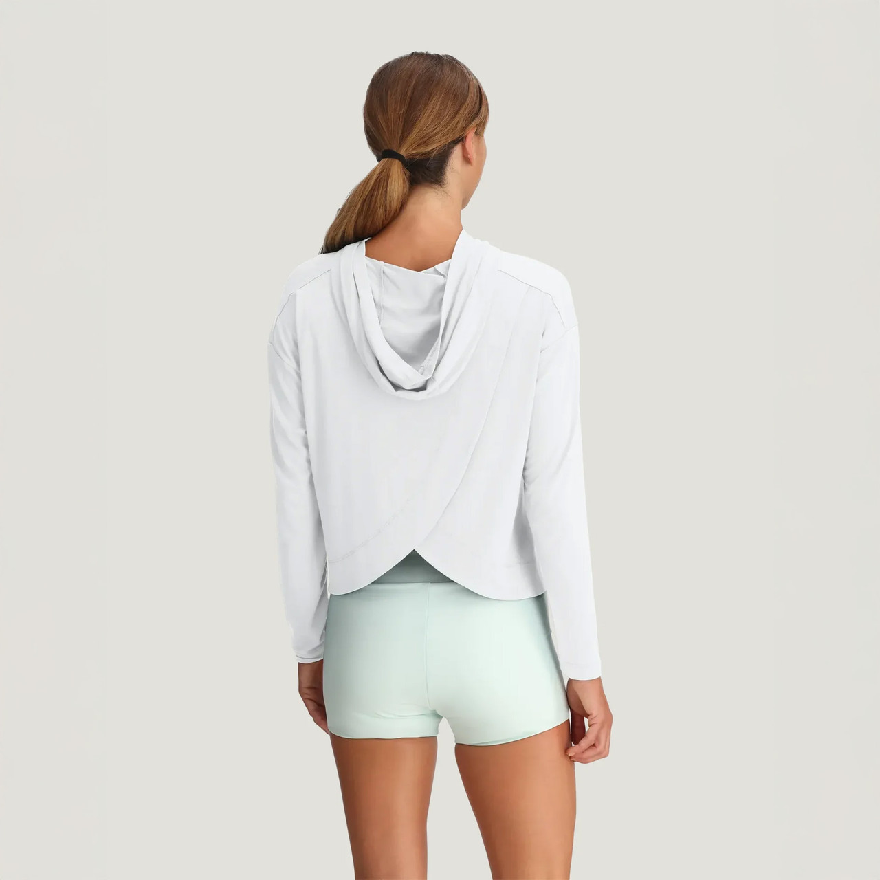 Free Fly Apparel Women's Bamboo Shade Crossover Hoodie, back view of a woman wearing a white bamboo crossover hoodie with long sleeves and a hood, paired with light mint shorts.