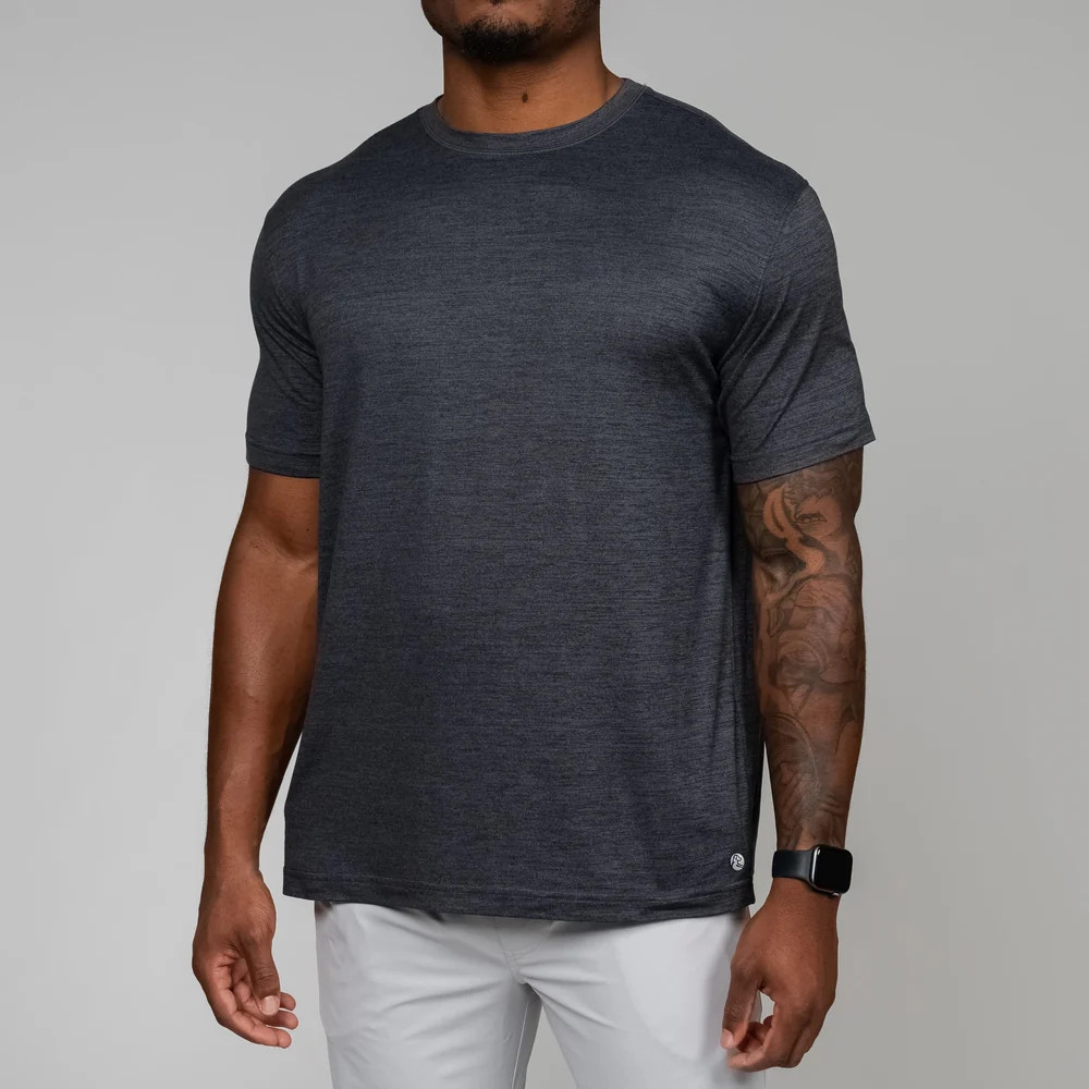 Rhoback Men's Tailwind Performance Tee, front view of a man wearing a dark gray athletic t-shirt with a subtle heather pattern and short sleeves, paired with white pants.