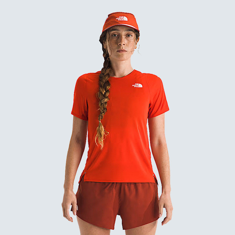 The North Face Women's Summit High Trail Short Sleeve, red athletic female model wearing a short-sleeve trail shirt with matching shorts and a red cap.