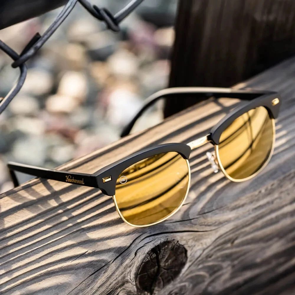 Knockaround Brooklines Sunglasses, stylish sunglasses with black frame and yellow-tinted lenses resting on weathered wooden surface.