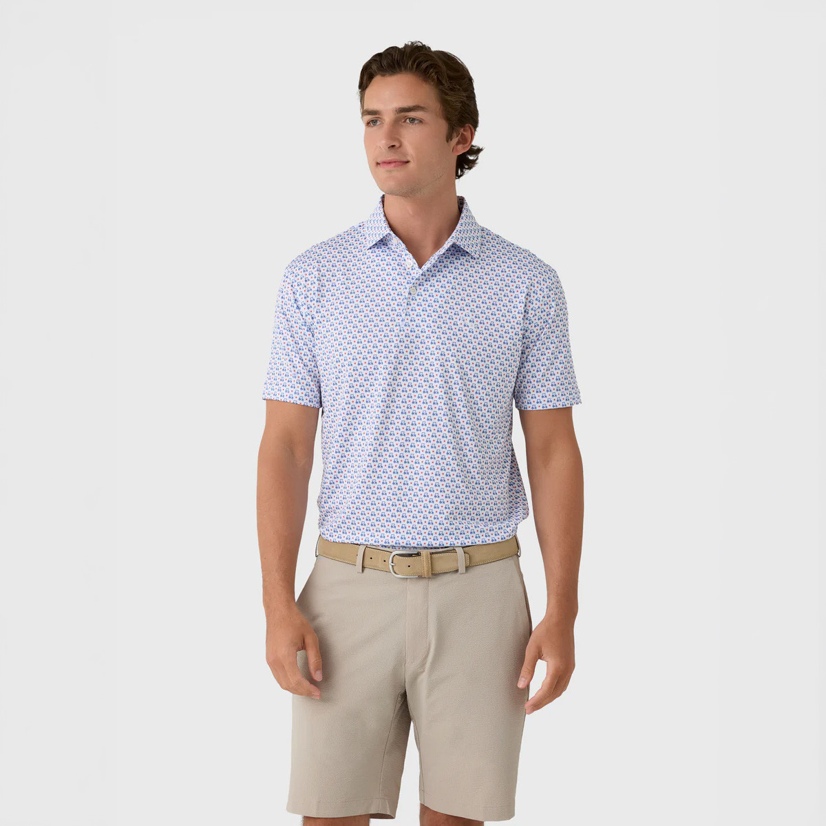 Rhoback Men's The Stars & Carts Performance Polo, a man wearing a stylish short-sleeve polo shirt with a colorful star and cart pattern, paired with beige shorts for a casual summer look.
