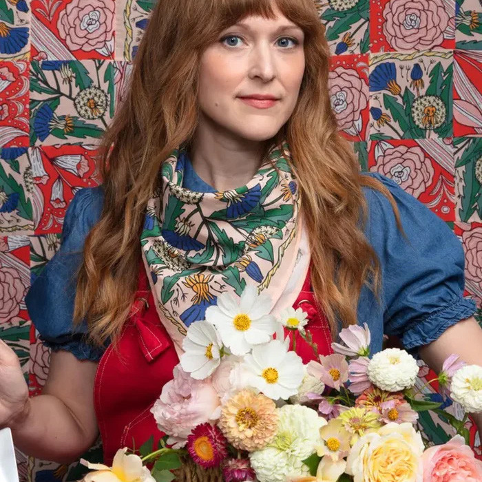 Handker Bandanas, floral printed fabric bandana worn around the neck by a woman with long red hair, holding a bouquet of colorful flowers, colorful floral patterned background.