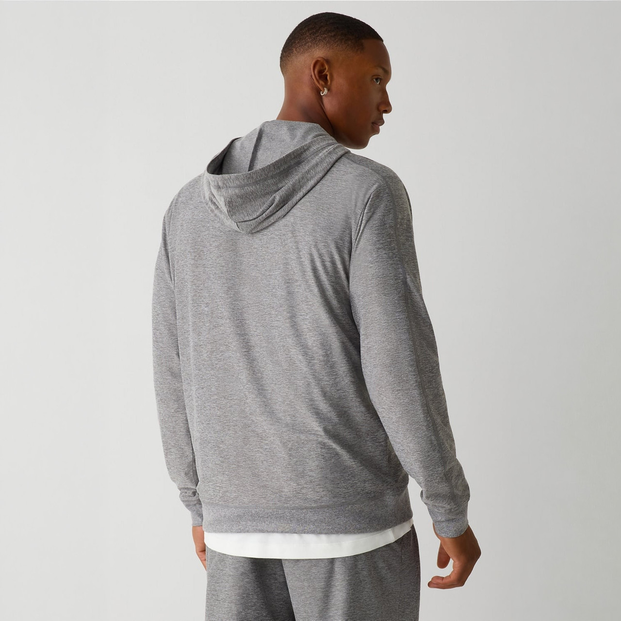 Fabletics The Cloud Jersey Hoodie, a man wearing a light gray hoodie with a subtle textured pattern, showing the back view.