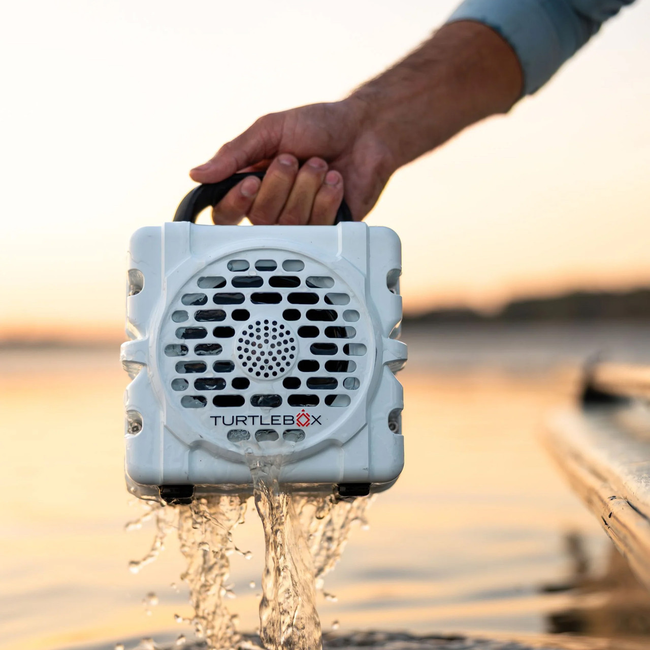 Turtlebox Audio Turtlebox Cub, portable waterproof speaker being held over water during sunset.