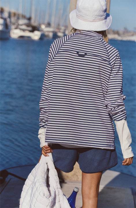 FP Movement Women's Restoration Yarn Dye Stripe Layer, model wearing striped jacket at a marina with boats in the background.