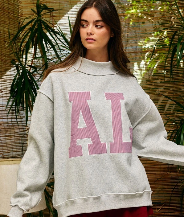 Bucketlist Women's AL Embroidered Mock Neck Sweatshirt, front view of a woman wearing a grey sweatshirt with pink embroidered 'AL' letters on the front, in a natural, outdoor setting.