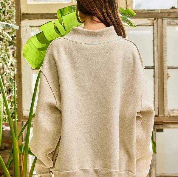 Bucketlist Women's Alabama Embroidered Mock Neck Sweatshirt, back view of a woman wearing a beige sweatshirt in a garden setting.