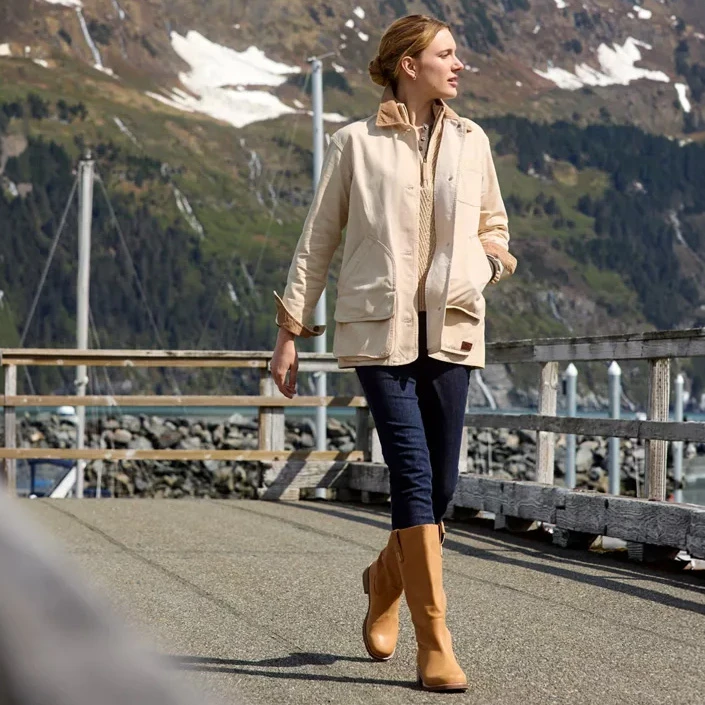 L.L.Bean Women's West End Boot, stylish tan knee-high boots paired with casual outdoor attire on a dock near water with mountains in the background.