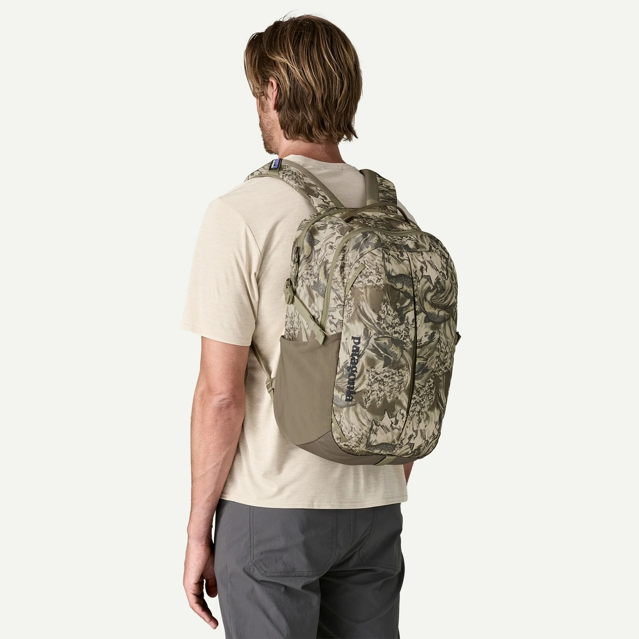 Patagonia Refugio Day Pack 26L, a man wearing a camouflage-patterned travel backpack with multiple compartments and adjustable straps.
