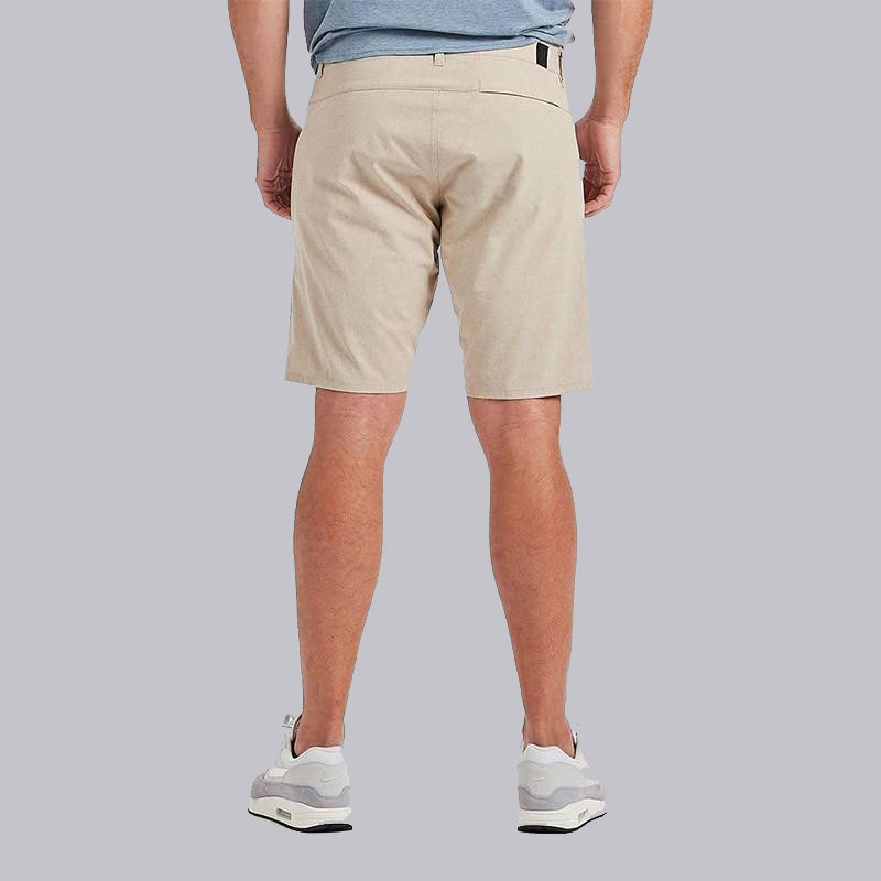 Vuori Men's Aim Short, a pair of beige men's casual shorts worn by a man standing against a light gray background.