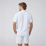 Vuori Men's Gamepoint Polo 2.0, a man wearing a white polo shirt and shorts, viewed from the back against a plain gray background.