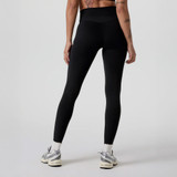 Vuori Women's AllTheForm Legging, image showing a woman from the back wearing black high-waisted leggings with athletic shoes on a plain background.