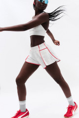Excluded Footwear Category FP Movement Women's Easy Tiger Short, a woman wearing white sports shorts with red piping, red sneakers, and grey socks, posing dynamically.