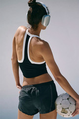 FP Movement Women's All Clear V-Neck Colorblock, image of a woman wearing a black and white sports crop top with colorblock design, paired with black athletic shorts, holding a soccer ball and wearing headphones.