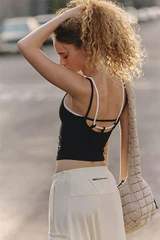 FP Movement Women's All Clear Coastline Cami, image of a woman wearing a black cami with stylish strappy back design and white pants, standing outdoors.