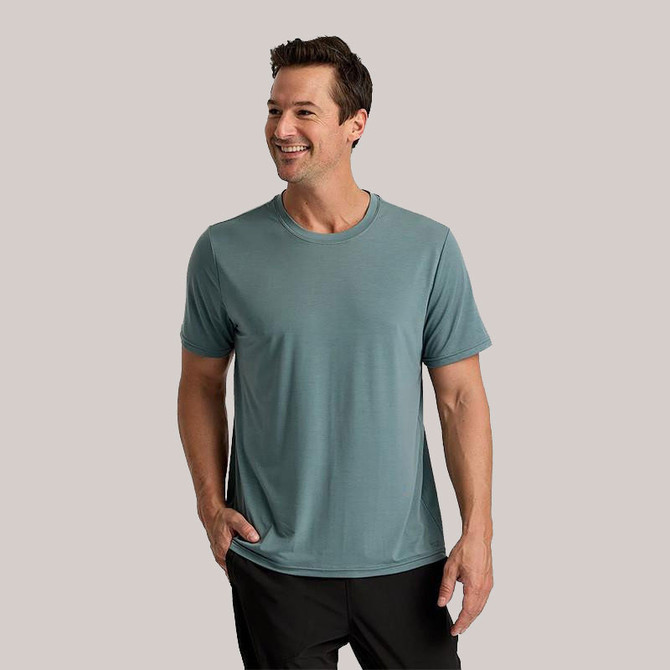 Free Fly Men's Short Sleeve Elevate Lightweight Tee, a man wearing a light blue athletic short sleeve t-shirt with a happy expression, casual pose on a plain background.