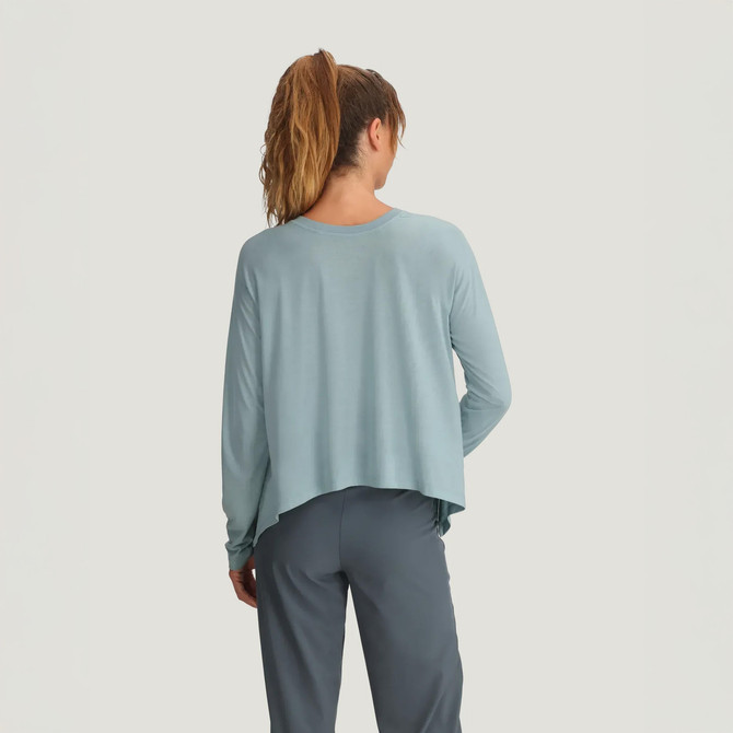 Free Fly Apparel Women's Bamboo Lightweight Cropped Long Sleeve, back view of a woman in a light blue cropped long-sleeve top with gray pants, showcasing the casual and comfortable design.