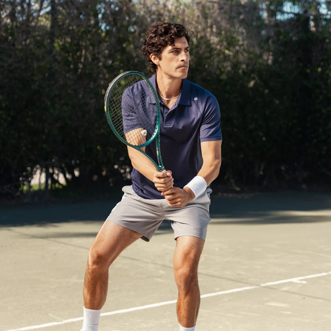Rhoback Men's Blitz Tech Polo, man playing tennis on outdoor court wearing navy blue sports polo and holding tennis racket.