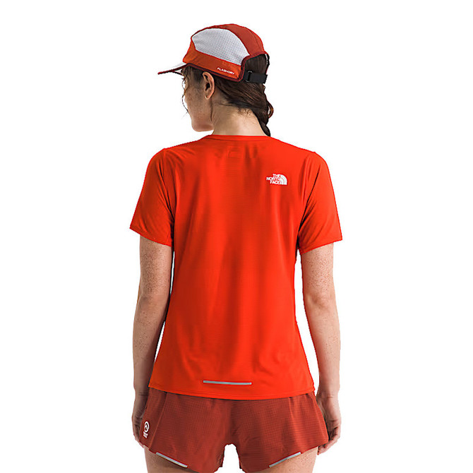 The North Face Women's Summit High Trail Short Sleeve, image of a woman wearing a bright red short sleeve athletic shirt and a red cap with a mesh panel.