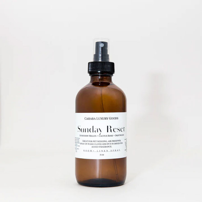 Cahaba Luxury Goods Room Spray, amber glass spray bottle with white label and black cap, labeled Sunday Reset with honeydew melon, cactus rose, and grapefruit scent.
