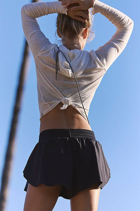 FP Movement Women's Element Short, product photo showing a woman wearing black athletic shorts with a flowy design, standing outdoors against a clear blue sky.