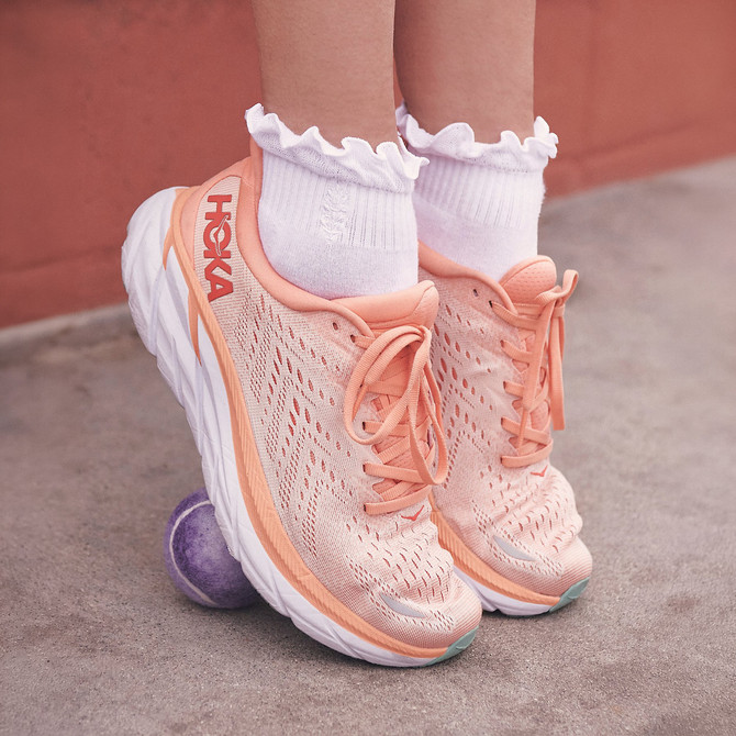 FP Movement Women's Classic Ruffle Sock, white ruffled ankle socks worn with peach athletic sneakers on a person's feet.