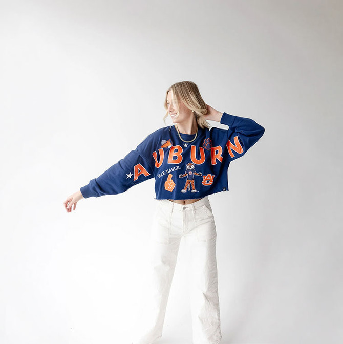 Gameday Social Apparel Gameday Social Auburn Patched Up Cropped LS Tee, model wearing a navy cropped long-sleeve Auburn sweatshirt with orange and white graphics and patches, styled with white jeans.