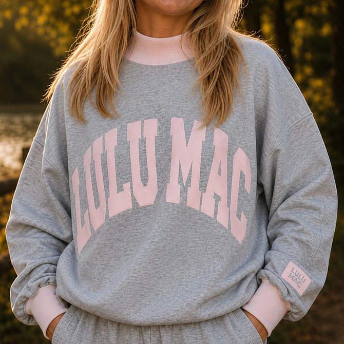 Lulu Mac LuluMac Women's Fan Favorites Puff Mock Neck Sweatshirt, woman wearing a gray textured sweatshirt with oversized pink Lulu Mac lettering, pink mock neck and cuffs, and relaxed sleeves.