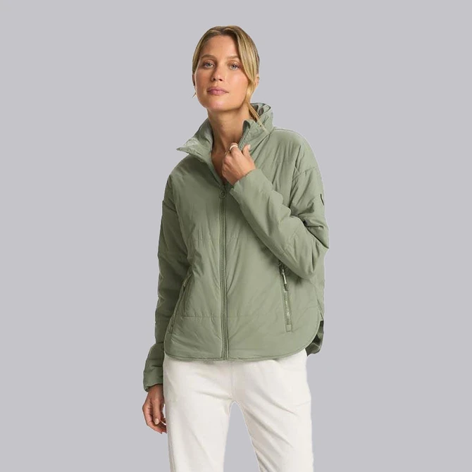 Vuori Women's Canyon Insulated Jacket, a light green insulated outdoor jacket worn by a woman with the collar zipped up.