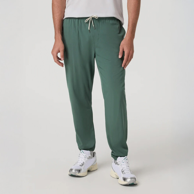 Vuori Men's Kore Jogger, green men's athletic joggers with drawstring waistband and tapered fit, paired with sneakers.
