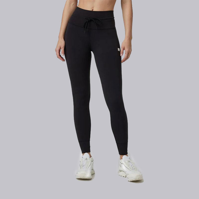 Vuori Women's AllTheFeels Legging, black high-waisted athletic leggings with a drawstring waist and slim fit, paired with white sneakers.