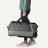 Patagonia Black Hole Wheeled Duffel 70L, a person holding a large grey rolling duffel bag with green handles and wheels, suitable for travel and adventure.