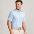 Tasc Performance Tasc Men's Cloud Polo Tiles, light blue men's polo shirt with a subtle geometric pattern, worn by a smiling man against a white brick wall background.