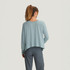 Free Fly Apparel Women's Bamboo Lightweight Cropped Long Sleeve, back view of a woman in a light blue cropped long-sleeve top with gray pants, showcasing the casual and comfortable design.