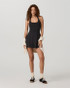 Vuori Women's Tiebreak Halter Dress, a woman wearing a stylish black halter dress with a fitted bodice and flared skirt, paired with casual socks and sneakers for a sporty yet fashionable look.