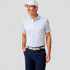 Johnnie-O Men's Performance Jersey Polo - Boggings, a man wearing a light-colored polo shirt with a subtle pattern, navy pants, a white cap, and a woven belt, standing against a plain background.