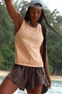 FP Movement Women's Hot Shot Twist Tank, a young woman wearing a sleeveless beige athletic tank top outdoors.