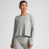 Beyond Yoga W's Featherweight Daydreamer Pullover, a light gray athletic sweatshirt worn by a woman with dark hair, featuring a relaxed fit and long sleeves with a classic crew neckline.