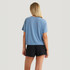 Free Fly Apparel Free Fly Women's Elevate Lightweight Tee, a woman wearing a light blue casual t-shirt with a relaxed fit and short sleeves, paired with black shorts against a plain white background.