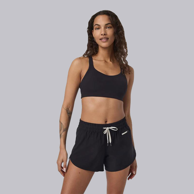 Vuori Women's Dynamic Bra, black sports bra worn by a smiling woman with wavy hair, styled for activewear comfort and support.