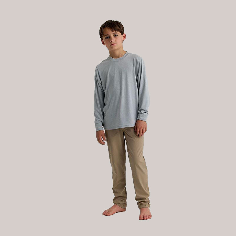 Free Fly Apparel Free Fly Youth Bamboo Shade Long Sleeve, a young boy wearing light gray long-sleeve shirt and beige pants, standing barefoot against a plain background.