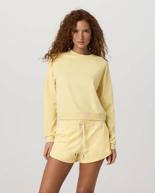 Vuori Women's Halo Modern Crew, woman wearing a pastel yellow long-sleeve sweatshirt and matching shorts for casual comfort and activewear style.