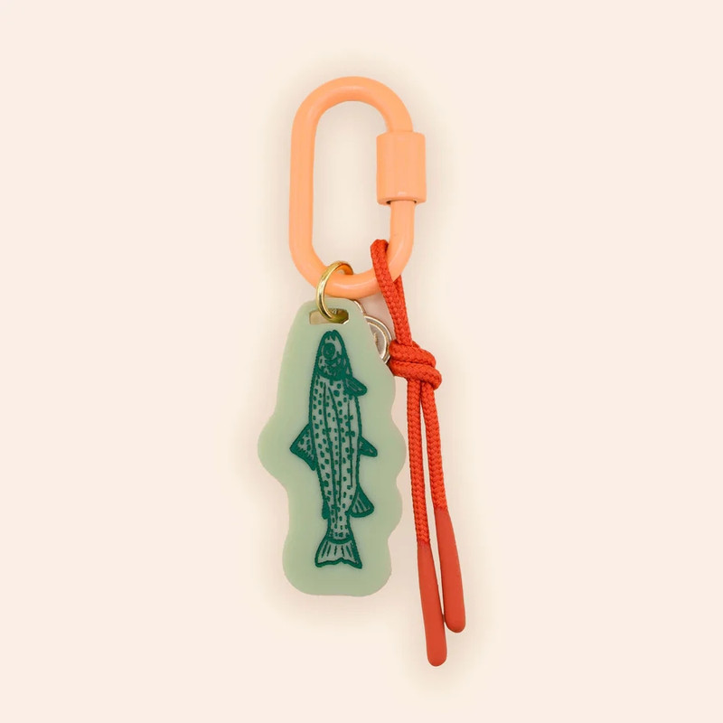 Freshwater Curated Goods Trout Fish Bag Charm, coral-colored carabiner with a green trout fish-shaped silicone keychain and red cord accessory.