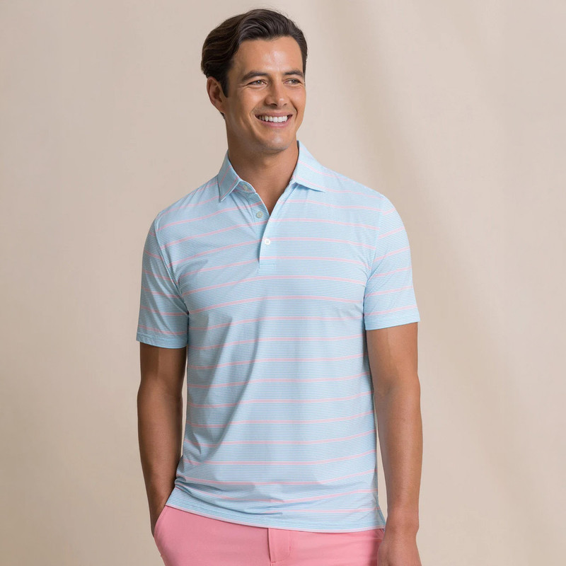 Southern Tide Men's Core Sound Stripe Coastal Breeze Performance Polo, a man wearing a light blue and pink striped polo shirt with a collar, smiling against a neutral background.