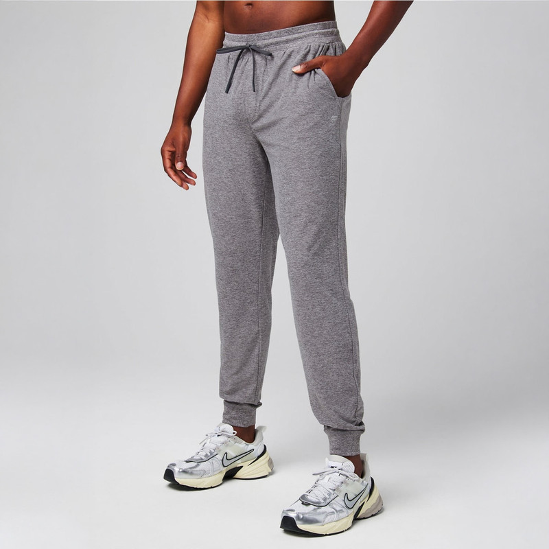 Fabletics Men's The Cloud Jersey Jogger, gray athletic jogger pants with a drawstring waistband and side pockets, worn with sneakers.