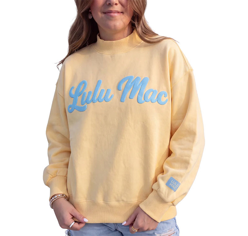 Lulu Mac Women's Script Sweatshirt, woman wearing a pale yellow crewneck sweatshirt with raised blue script logo and matching sleeve detail.