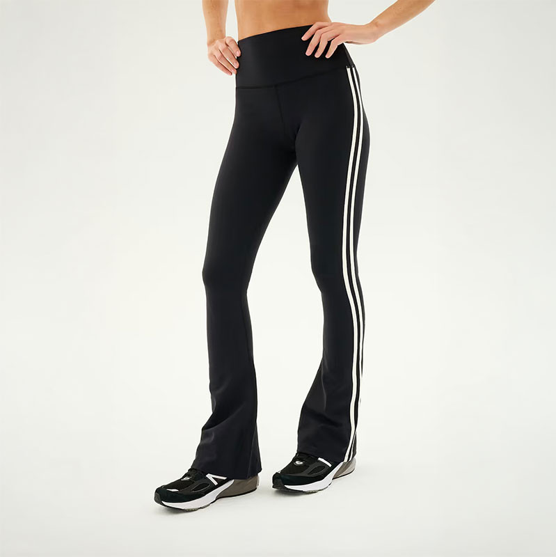 Splits59 Women's Raquel High Waist Double Stripe Supplex Flare 32 in, model wearing black high-waisted flared leggings with double white side stripes and sneakers.