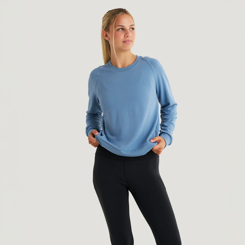 Free Fly Apparel Women's Bamboo Lightweight Fleece Crew, woman wearing a light blue fleece sweatshirt with long sleeves and a relaxed fit, standing against a plain white background.