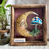 Charming is a handmade clay sculpture featuring a peaceful crescent moon face and whimsical mushroom, displayed in a handcrafted wooden frame with its own unique inspirational label.