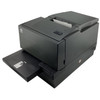 An angled front view showing the top, front, and right side of the dark charcoal POS printer. A flat black check-validation tray extends forward from the lower left side, detailed with an icon showing correct check orientation. The top of the printer features a main receipt paper exit slot with a small white piece of paper sticking out, alongside a rectangular paper feed button. The circular NCR logo is printed on the front-left corner.